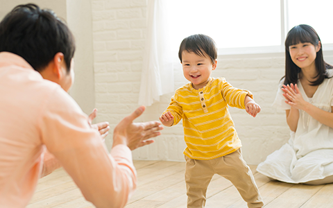ひとりで歩けるようになった男の子とそれを見守る両親